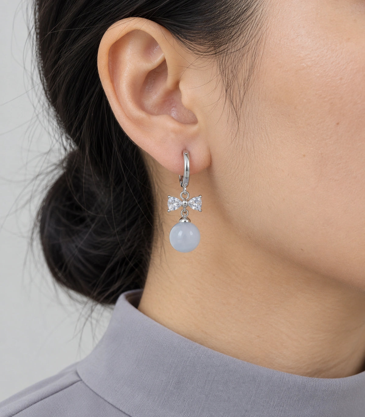 JIMIKI Silver-Tone Clear Crystal Bow Pale Blue Bead-Drop Huggie Earrings in Silver / Clear / Pale Blue, model wearing view
