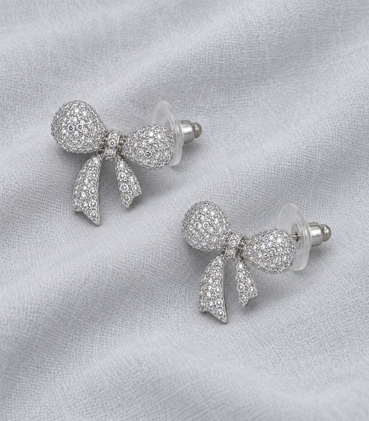 JIMIKI Pave Ribbon Bow Stud Earring Pair in Silver-tone, editorial flat lay #color_silver-tone
