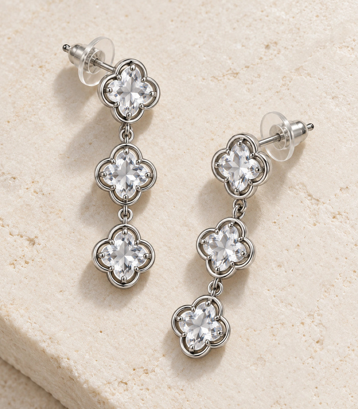 JIMIKI Triple Quatrefoil Crystal Drop Earring Pair in Silver tone / clear, editorial flat lay #color_silver tone / clear