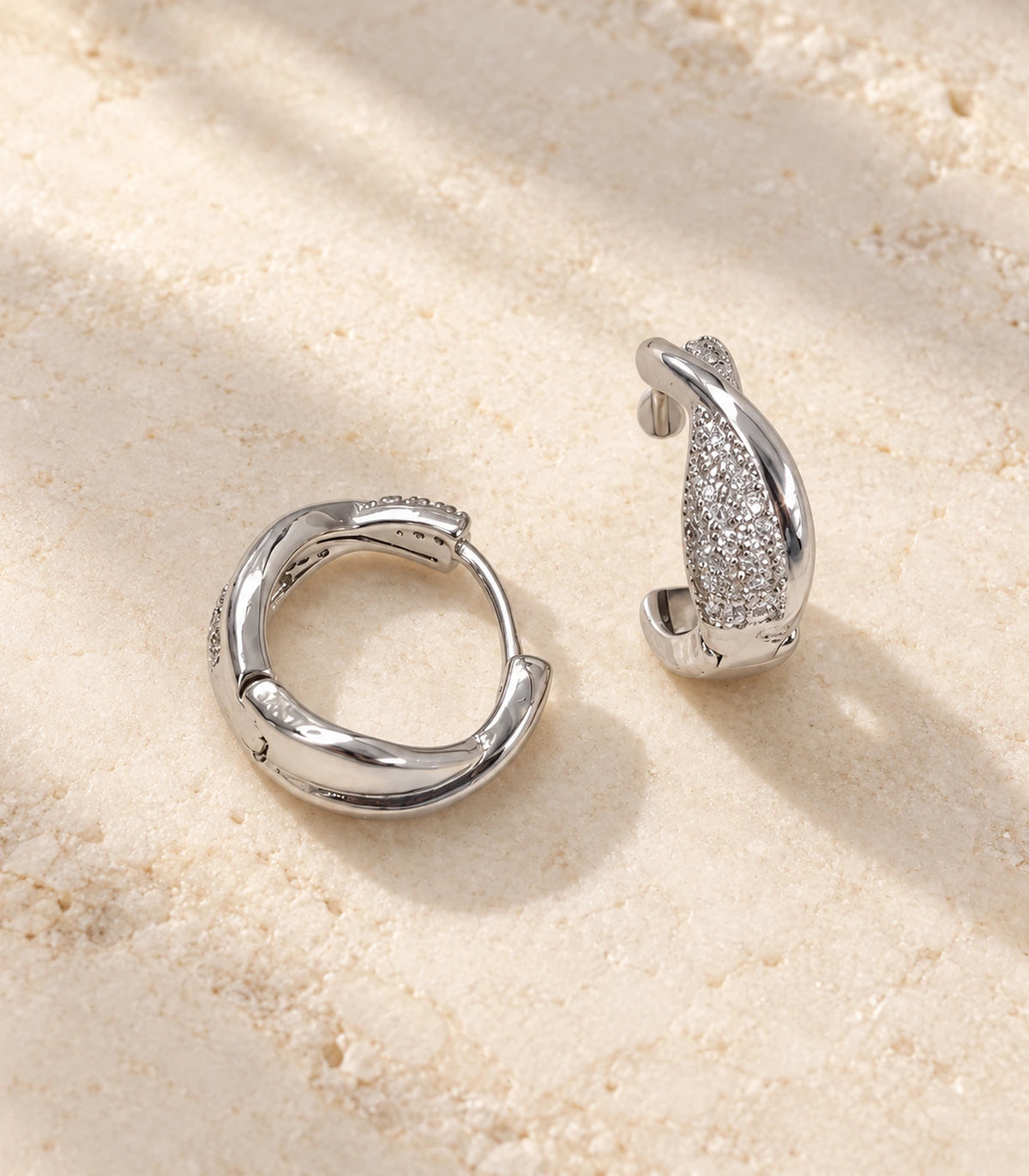 JIMIKI Silver crossover pave huggie hoop earrings, pair arranged on textured stone #color_silver