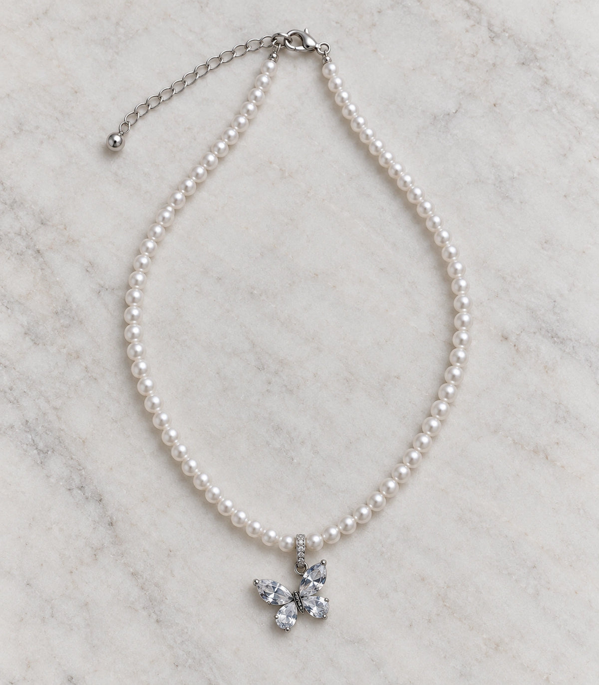 JIMIKI Silver-Tone Crystal Butterfly Pearl Necklace in Silver-tone / clear / white, arranged in an editorial flat lay