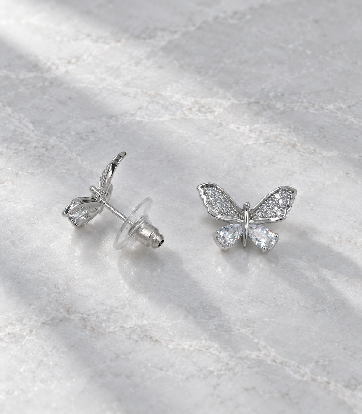 JIMIKI Silver-Tone Crystal Butterfly Stud Earrings in Silver / Clear, editorial flat lay