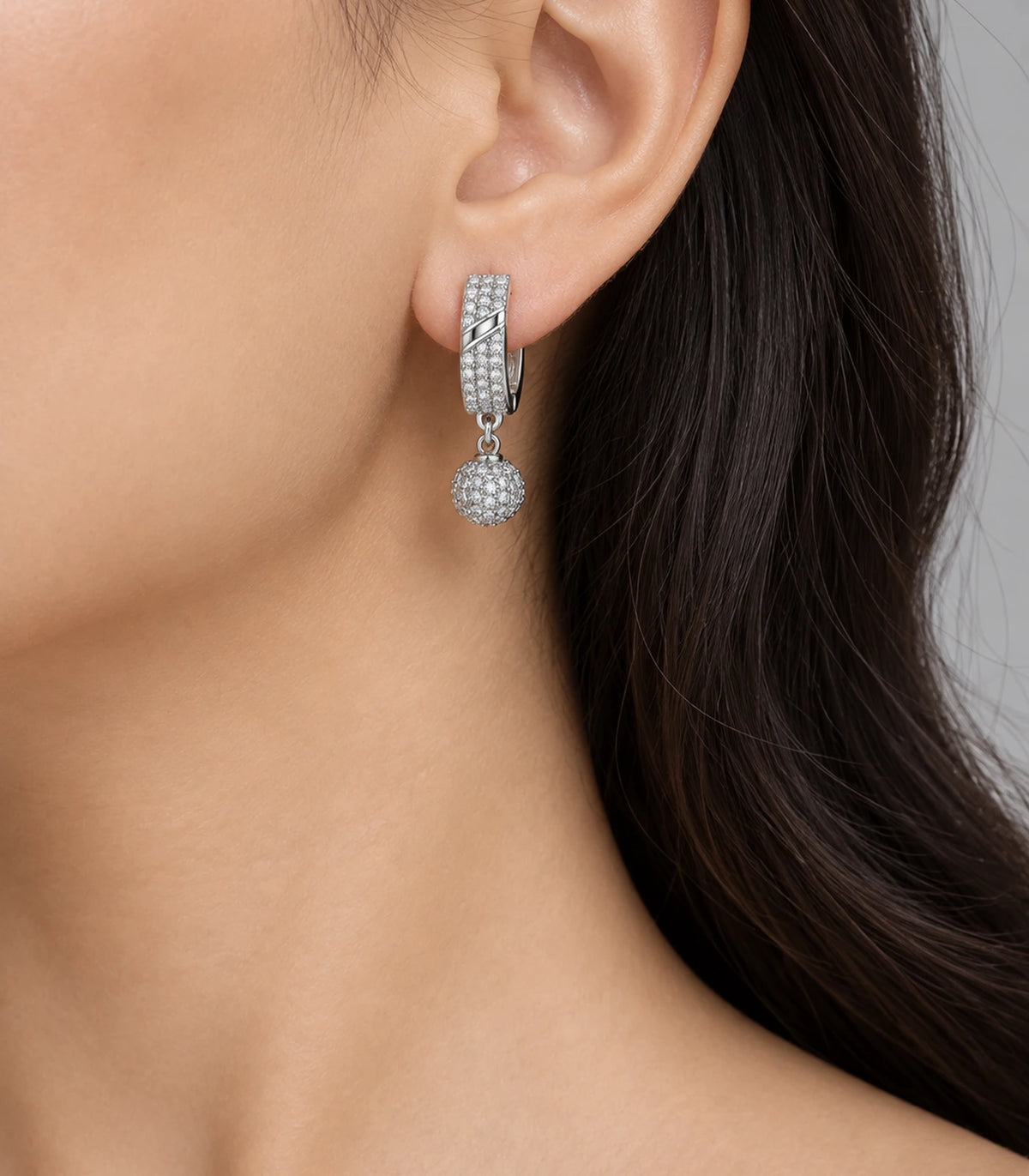 JIMIKI Silver-Tone Diagonal Pavé Ball Drop Huggie Earrings — worn on the ear #color_silver-tone / clear