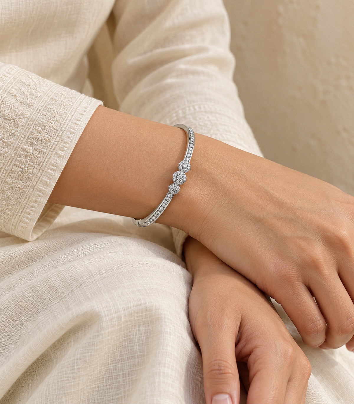 Silver-tone crystal flower bangle worn on a wrist resting over an ivory-clad lap