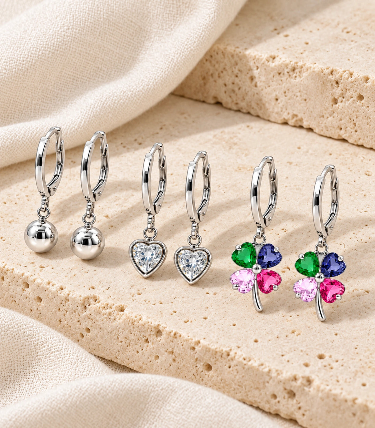 Complete silver-tone three-pair hoop earring set: ball, clear heart crystal and multicolour clover pairs — editorial-flatlay