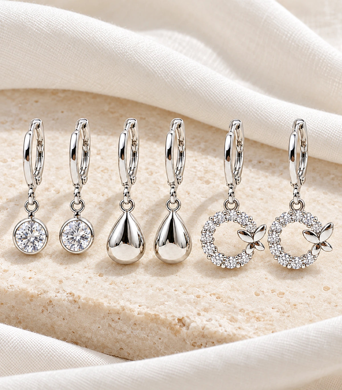 All six silver-tone earrings arranged on pale fabric and stone