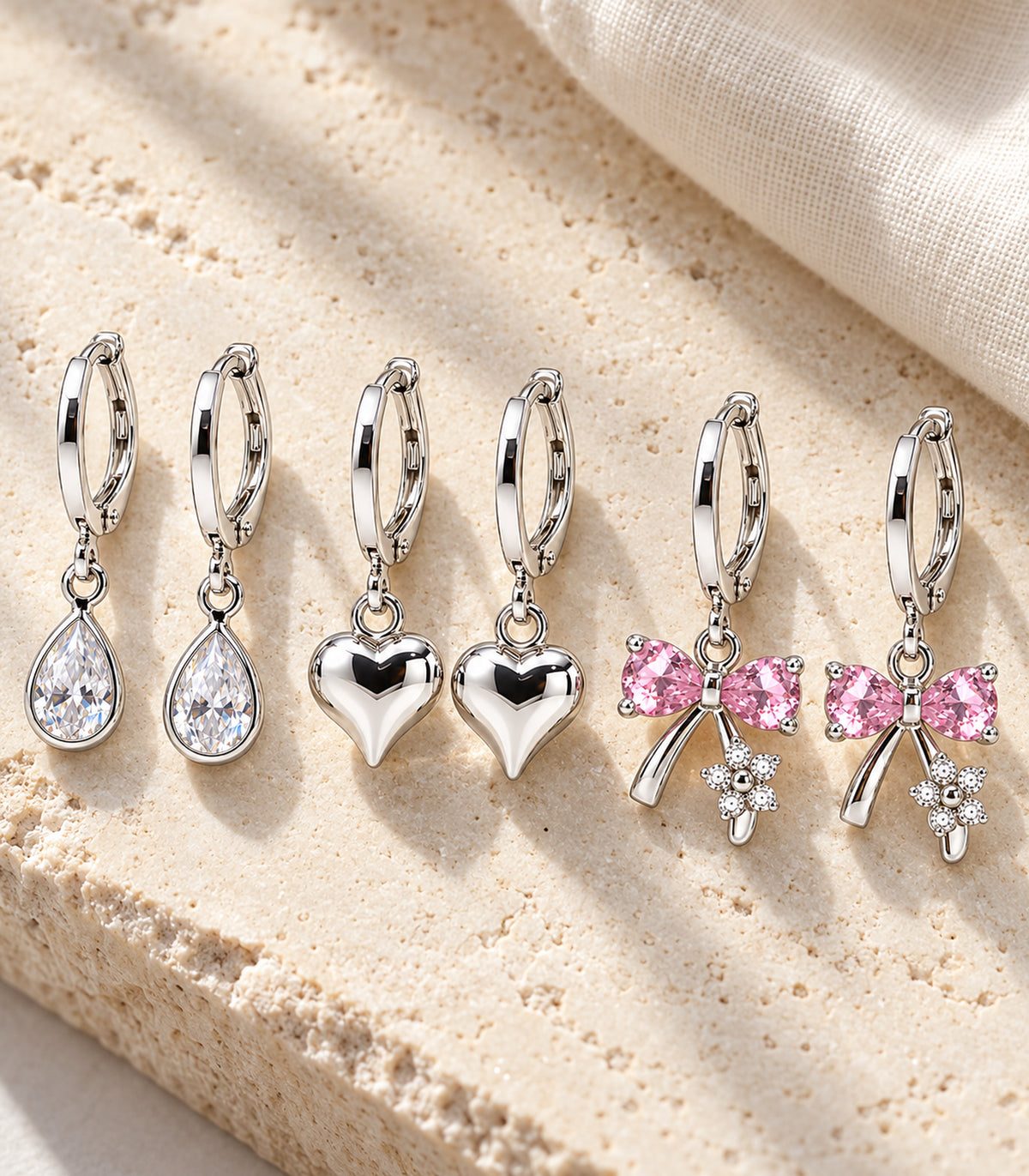 All three matching pairs of silver-tone charm hoop earrings arranged on pale stone