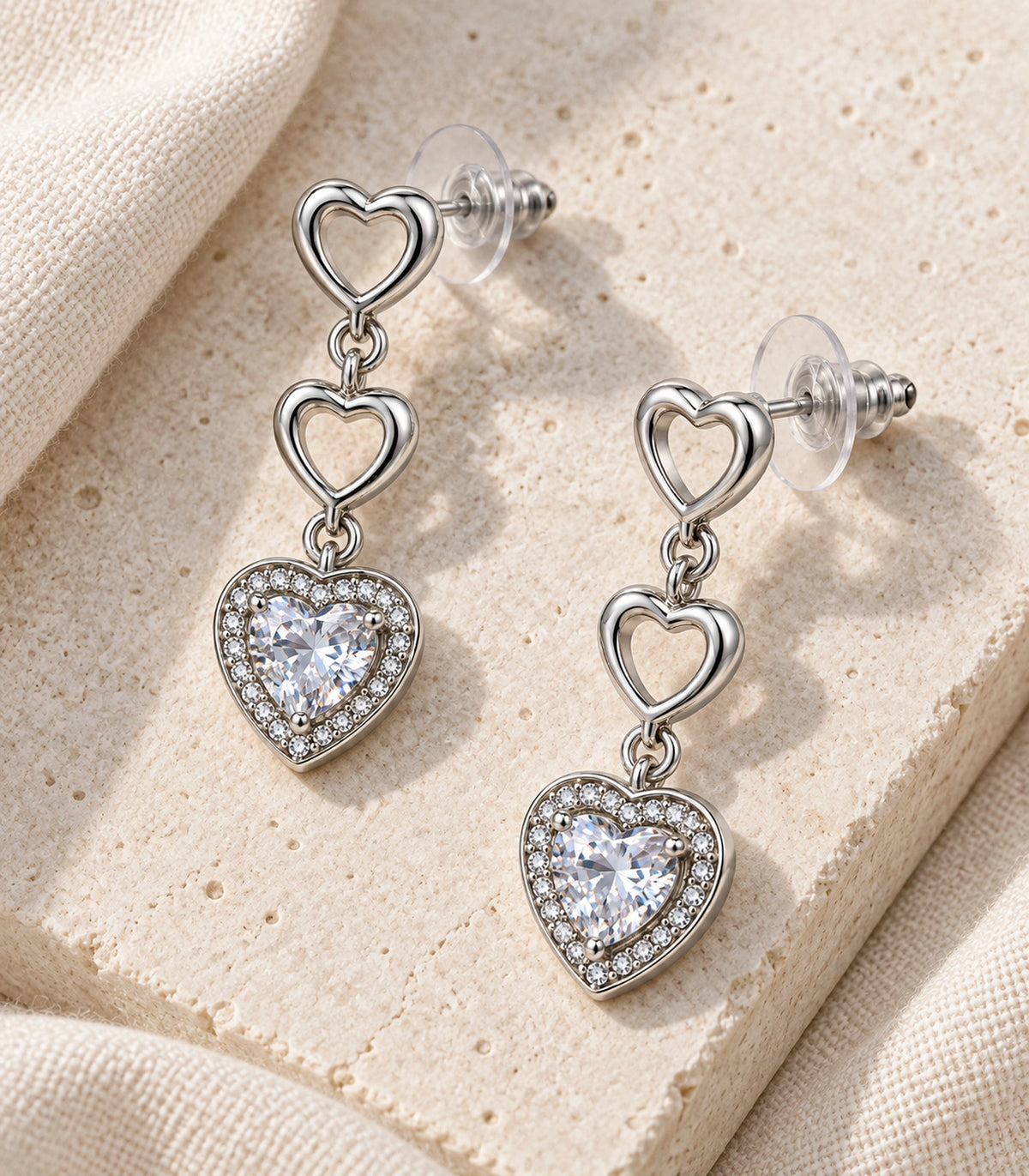 JIMIKI Triple Heart Crystal Drop Earring Pair in Silver tone / clear, editorial flat lay #color_silver tone / clear