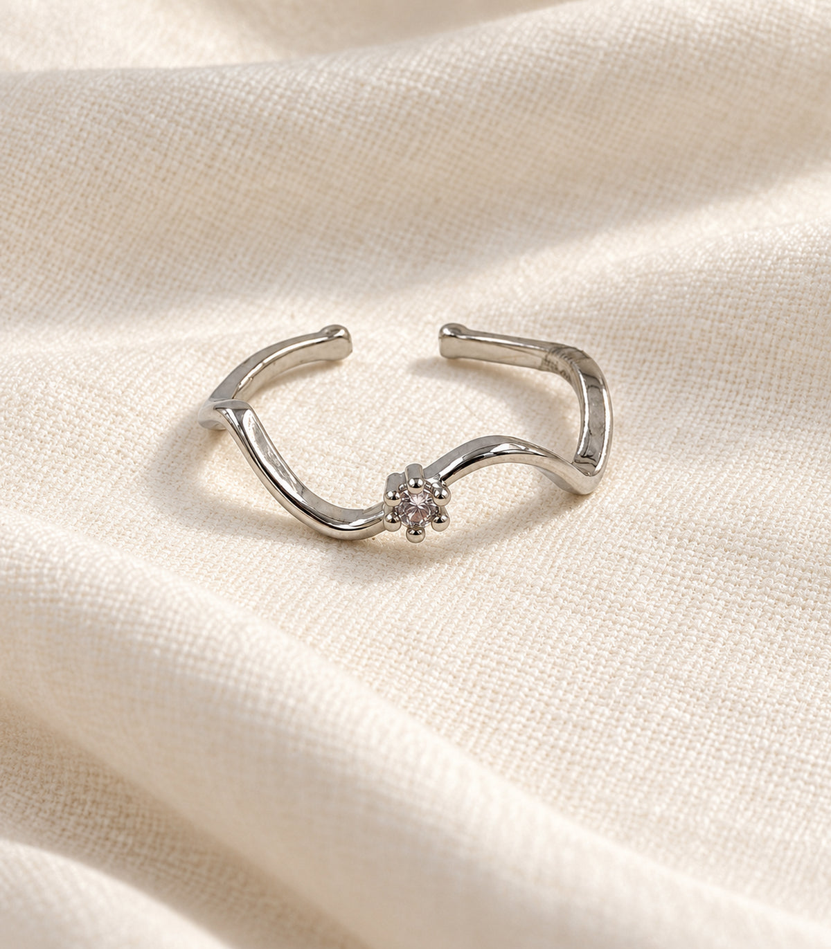 Silver-tone open wave ring arranged on ivory linen