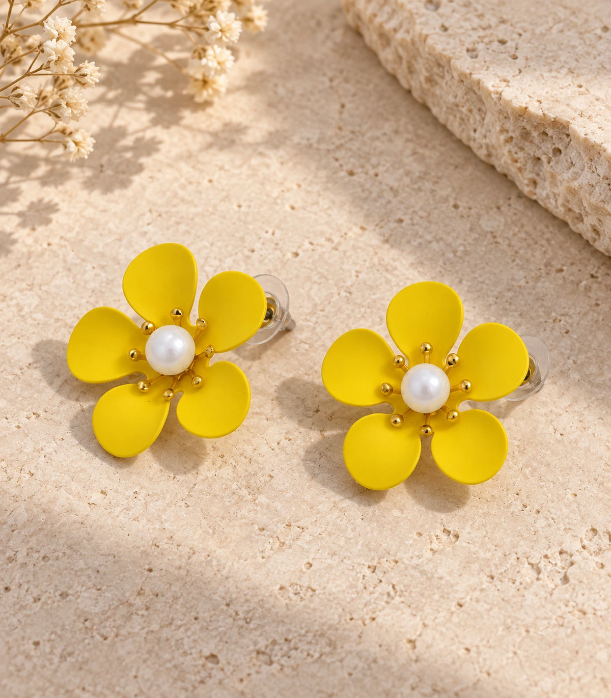 JIMIKI yellow five-petal flower stud earrings with pearl-effect centre, matching flower stud pair in an editorial flat lay #color_yellow