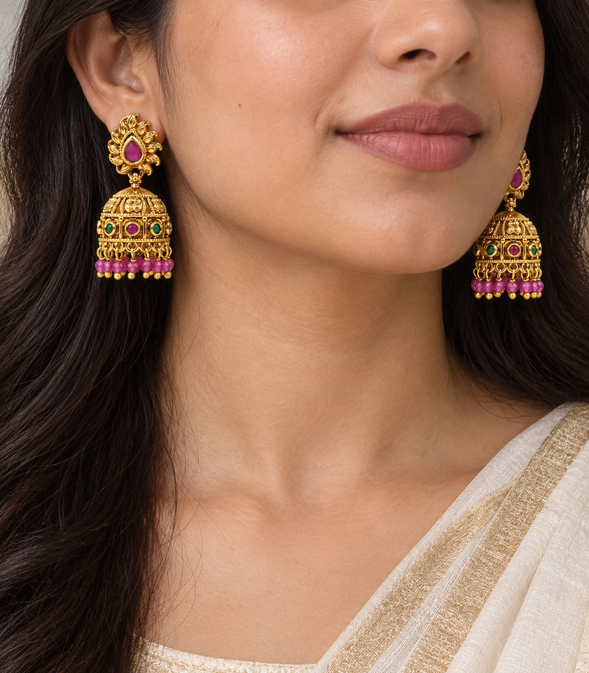 Worn close-up of magenta teardrop flame studs and ornate gold-tone jhumka domes