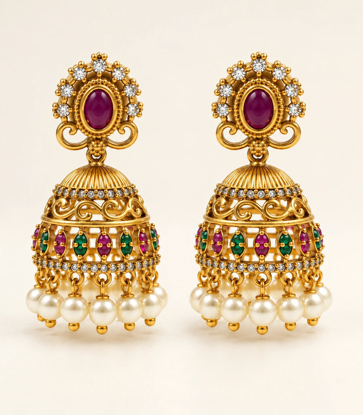 Matching antique gold-tone magenta and green pearl jhumka pair on a cream background