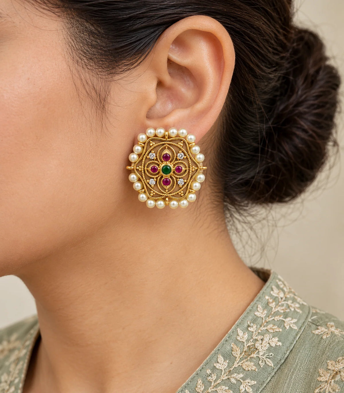 Close worn view of scalloped gold-tone studs showing magenta petal stones, green centres and pearl borders