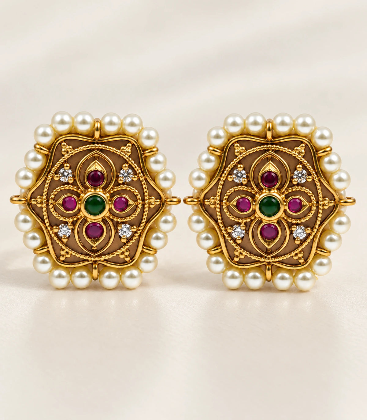 Complete matching pair of magenta and green gold-tone pearl-border stud earrings on cream fabric