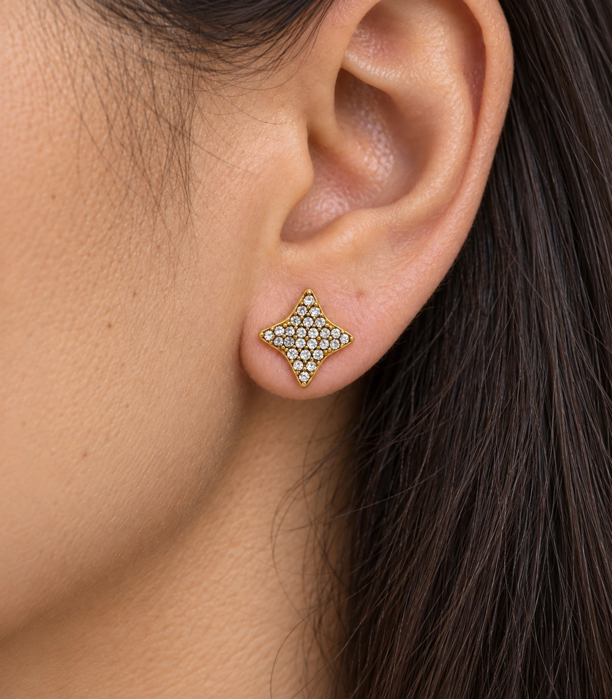 JIMIKI antique gold-tone four-point star stud earrings, macro worn view of the clear stone pattern and gold-tone rim #color_antique-gold