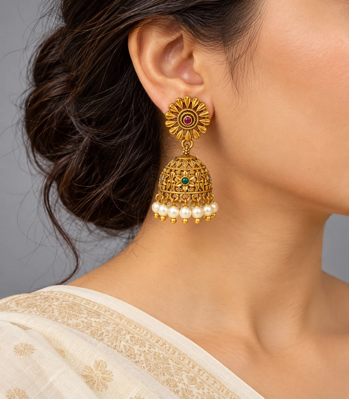 Antique gold tone sunflower jhumka earrings worn with cream and gold drape, showing magenta centres, green floral bells and pearl fringe