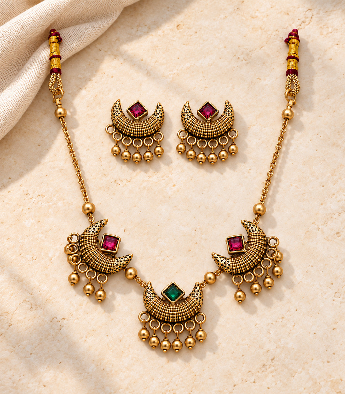 Complete antique gold-tone magenta green crescent necklace and matching earring pair arranged on linen