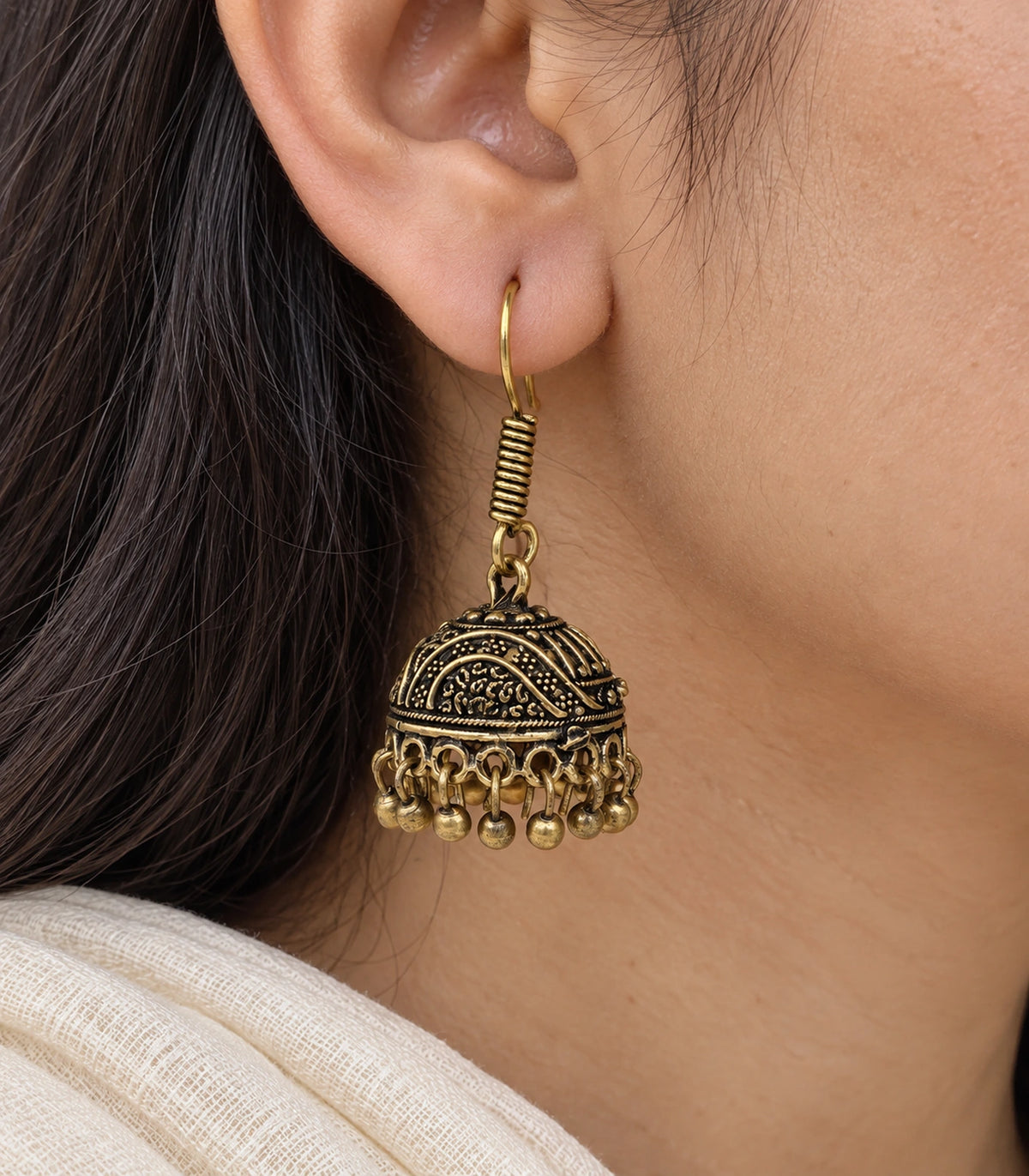 Close-up of raised wave scroll detail and round fringe on an antique gold-tone jhumka #color_antique-gold