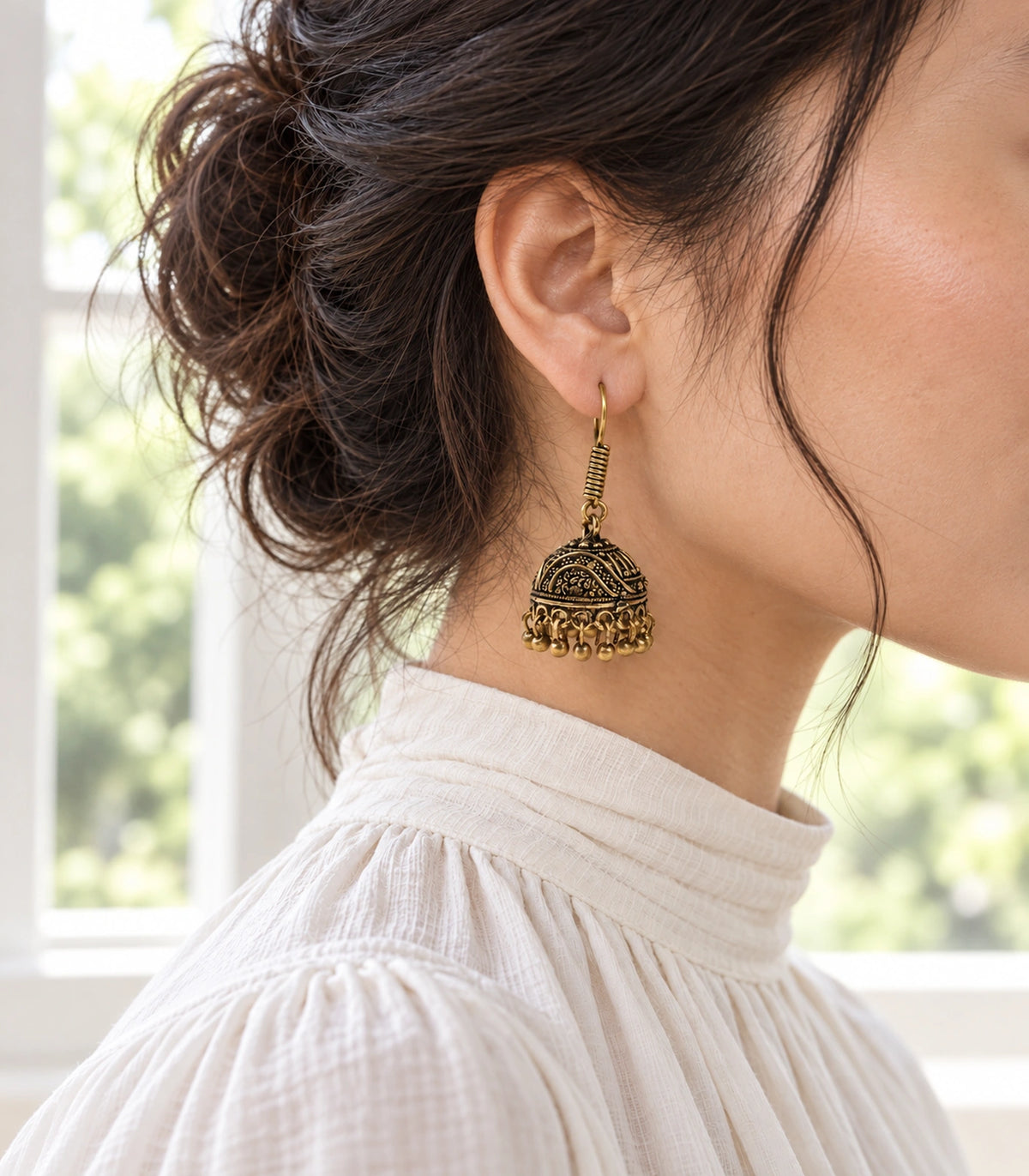 Editorial side view of an antique gold-tone wave scroll jhumka worn with hair tied back #color_antique-gold