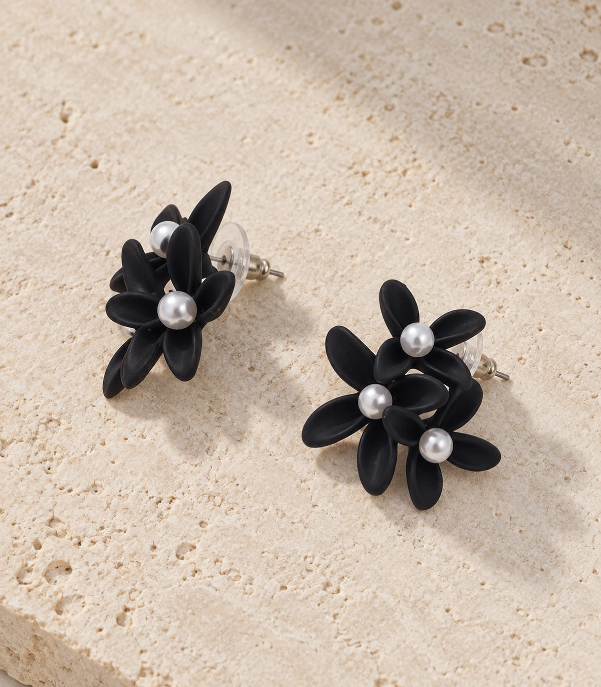 JIMIKI Black cascading floral cluster stud earrings, matching pair styled on a light textured surface #color_black