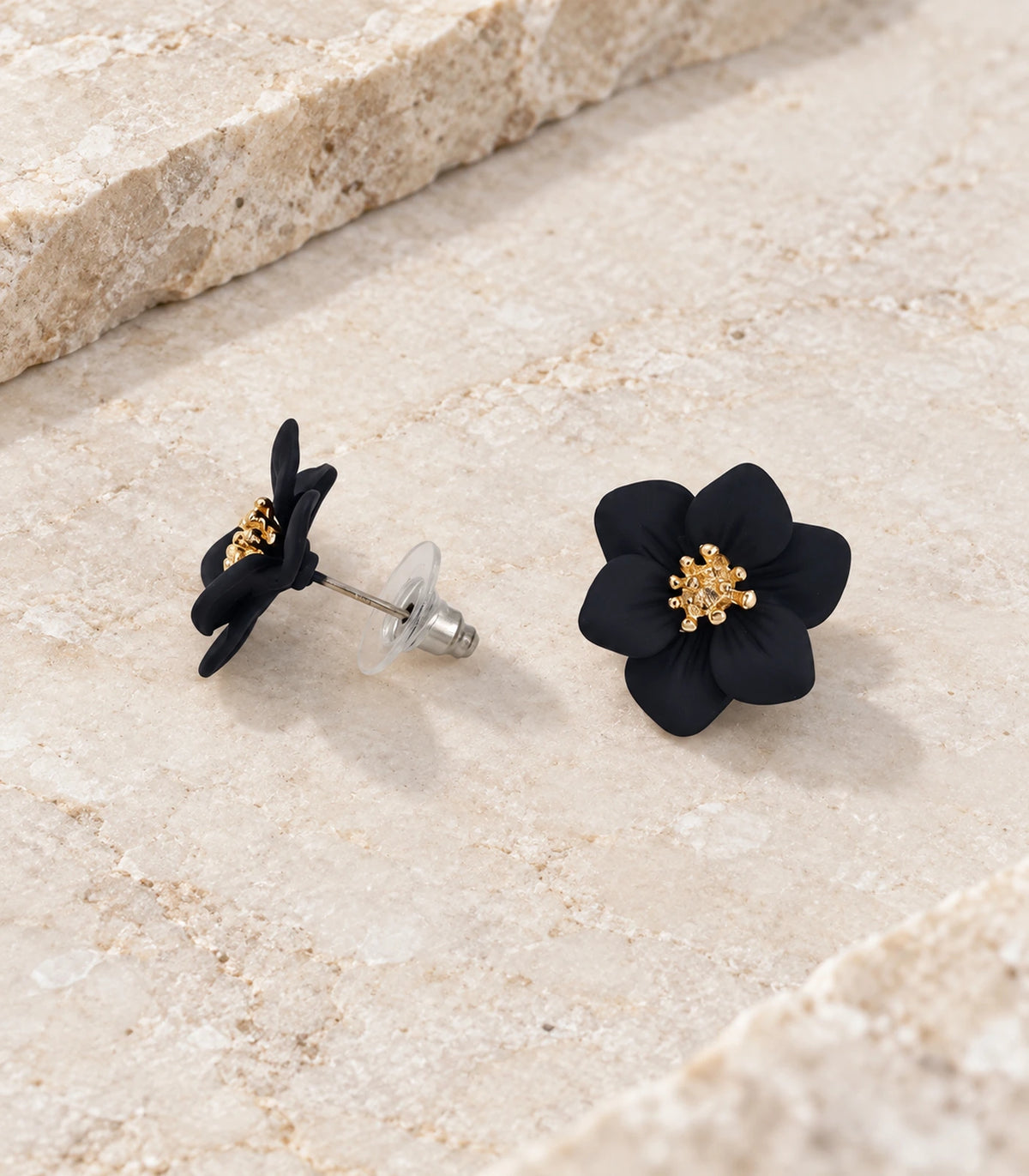 JIMIKI Black compact six petal flower stud earrings, matching pair in a styled flat lay #color_black