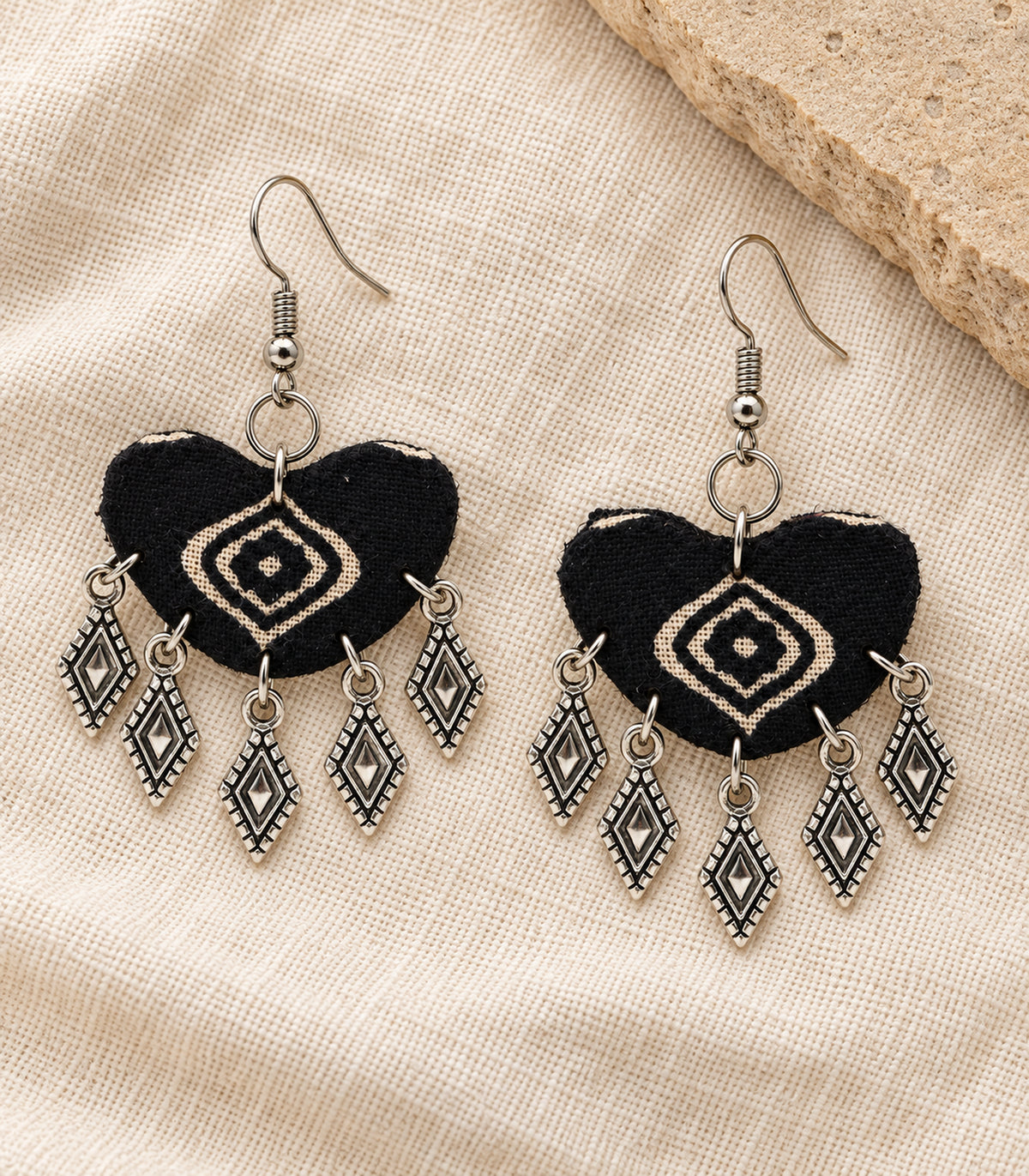 Complete pair of black fabric charm earrings arranged on neutral linen