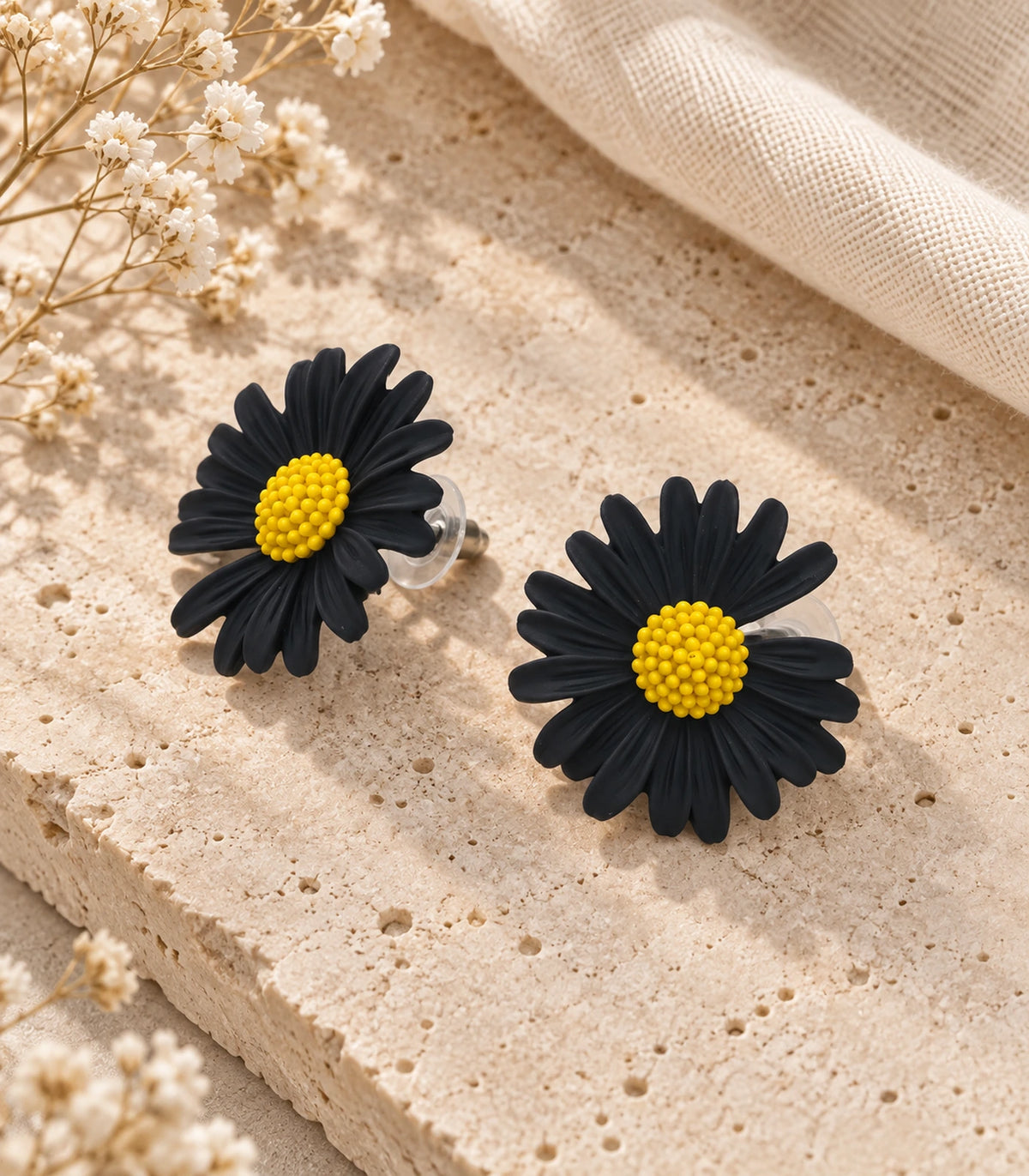 JIMIKI Black yellow centre daisy stud earrings, matching pair on a styled stone surface #color_black