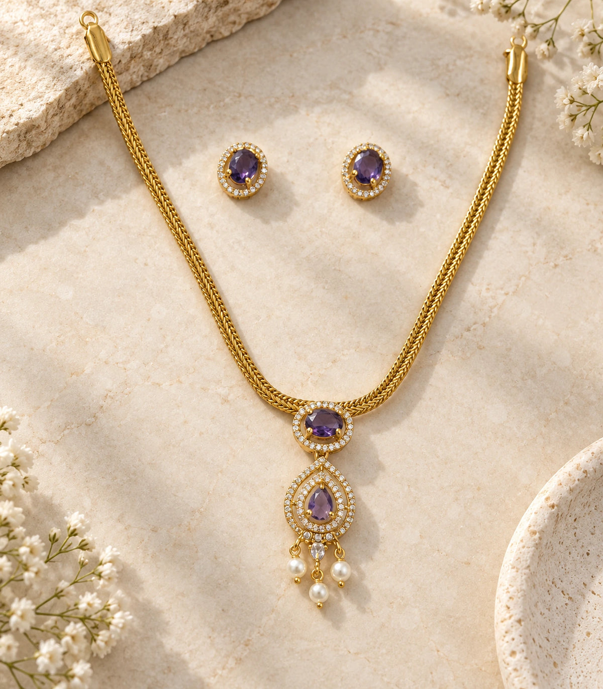 Complete gold-tone purple necklace and matching pair of oval stud earrings arranged on a light stone background