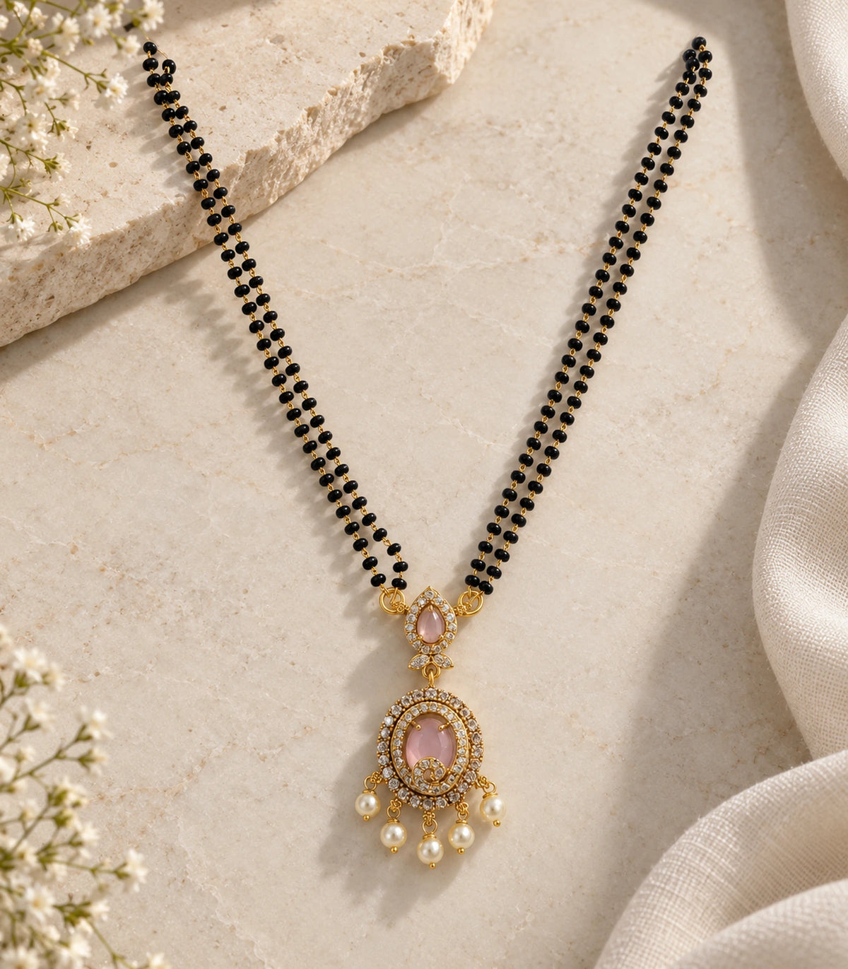 Single gold-tone blush pendant necklace with double black-bead strands and five pearl drops on stone and linen