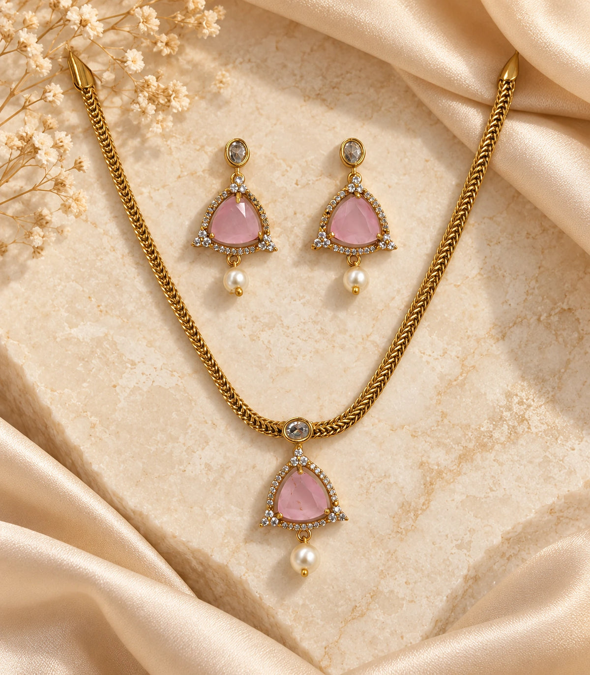Gold-tone blush pink necklace and two matching earrings arranged on a textured surface