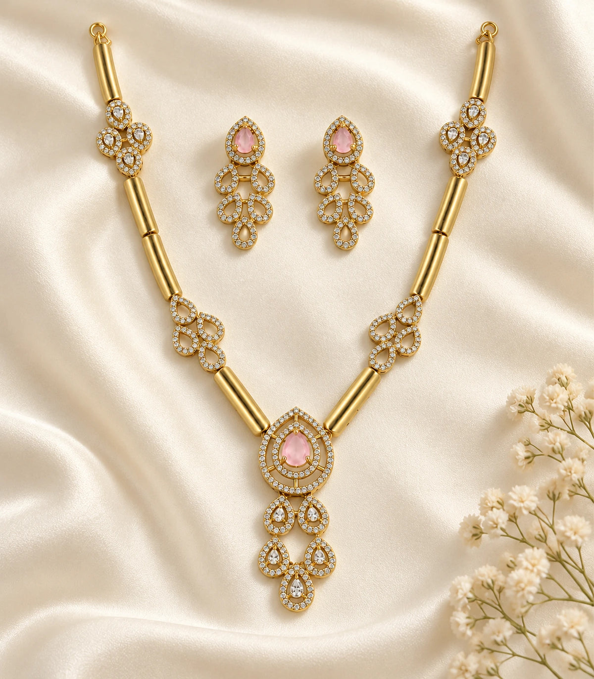 Complete gold-tone blush necklace and two earrings arranged on ivory fabric