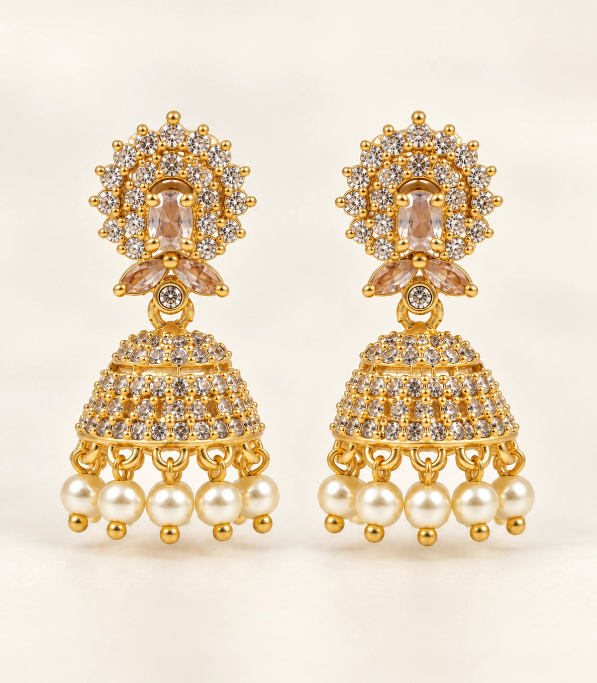 Complete champagne and clear gold-tone jhumka earring pair on a warm neutral surface