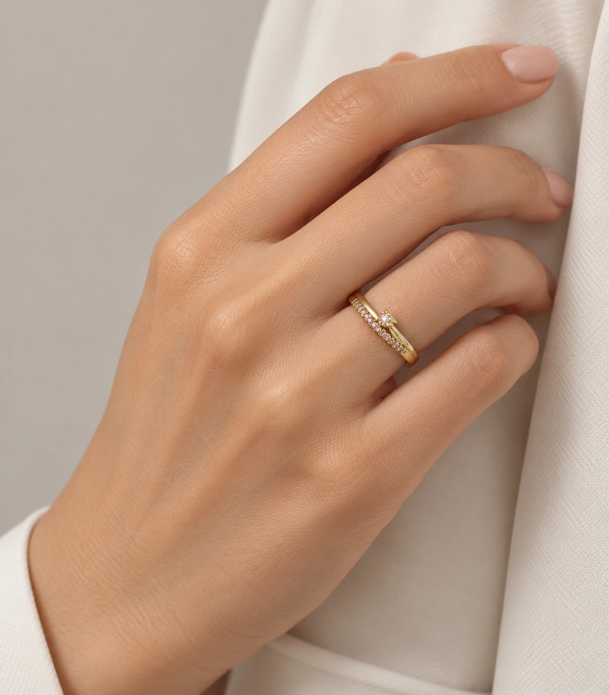 Gold crystal wishbone arrow ring worn on a finger beside a cream sleeve
