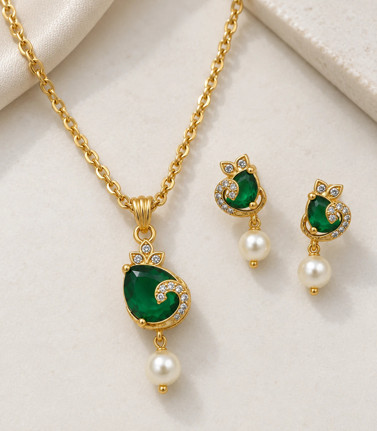 Detail of emerald-green pendant and matching earrings with clear accents and pearl-look drops on cream fabric