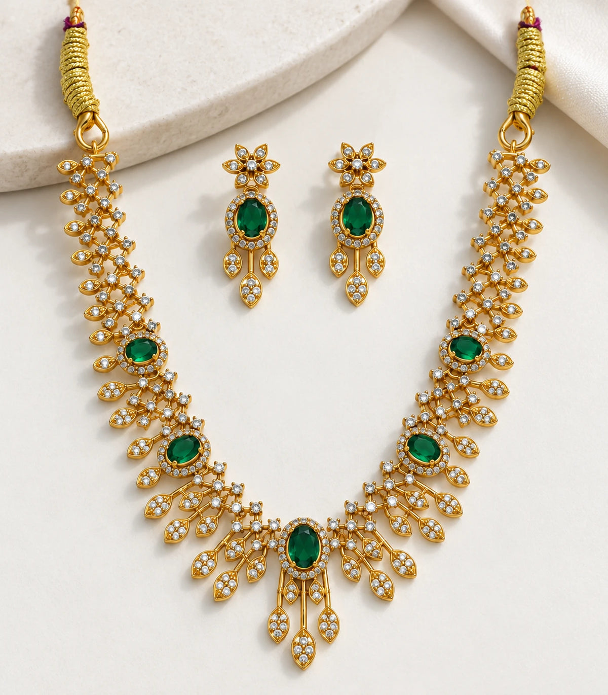 Close view of the necklace and matching floral drop earrings on pale fabric