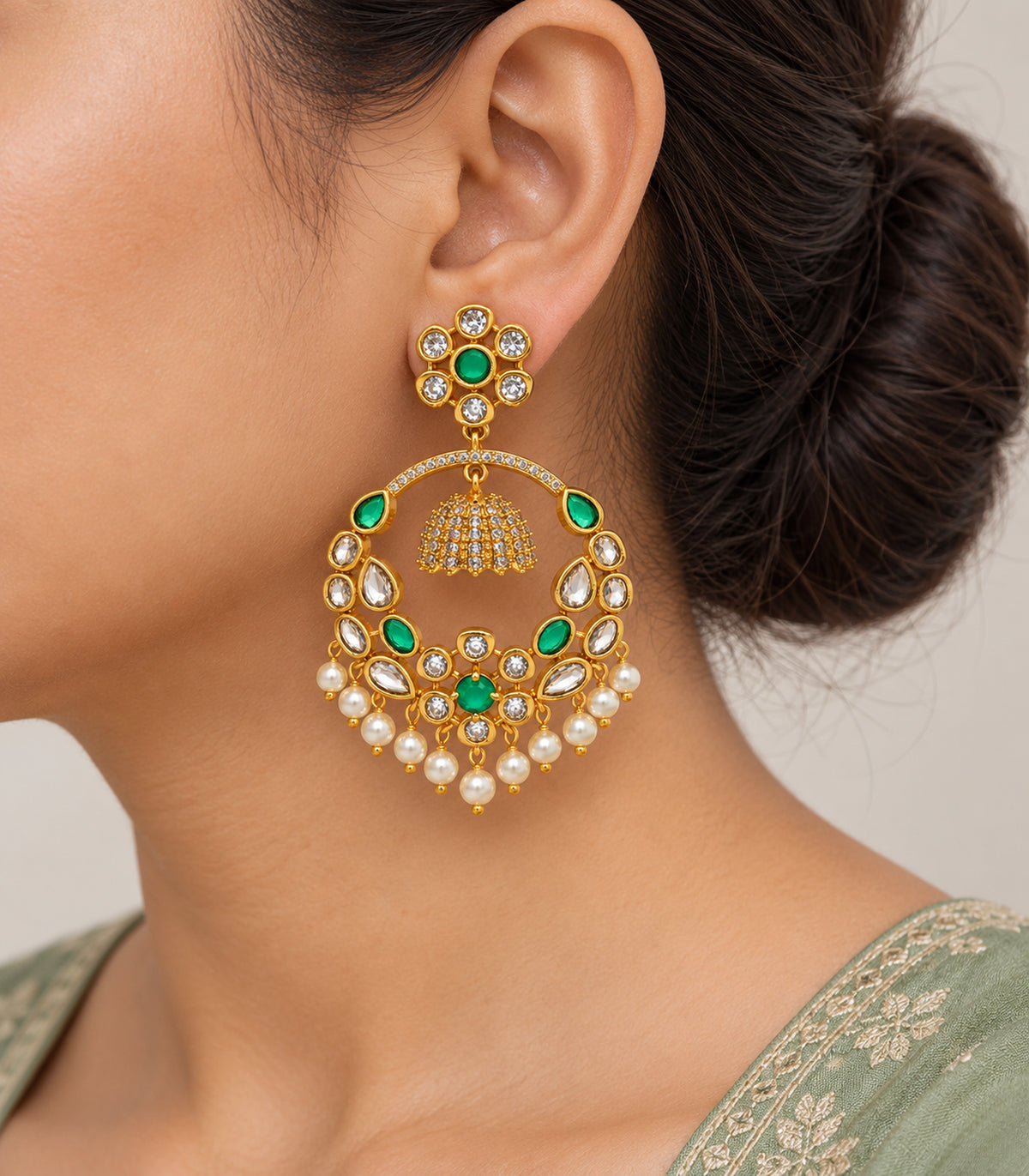 Close view of one gold-tone green floral chandbali earring with suspended mini bell and eleven white pearl-like drops