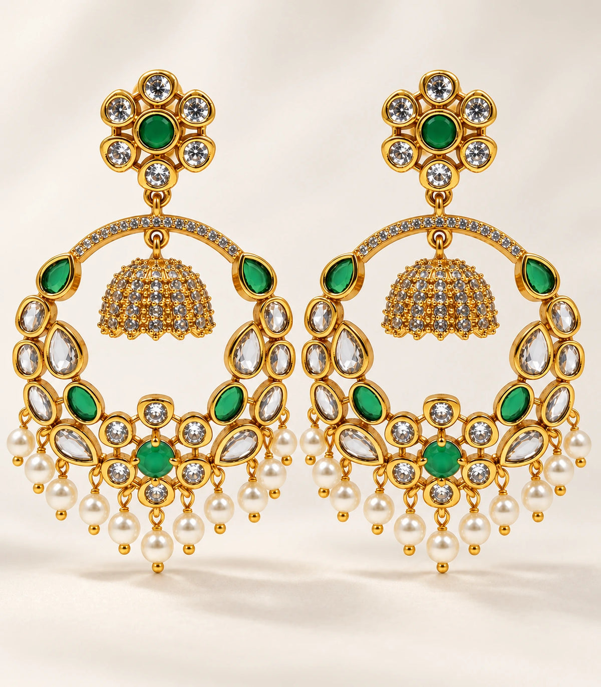Complete matching pair of gold-tone green and clear chandbali earrings with white pearl-like fringe on neutral fabric