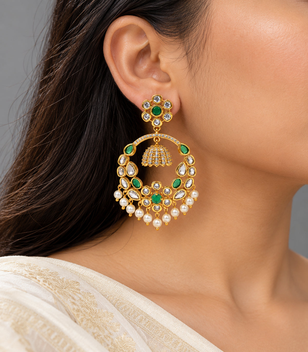 Gold-tone green and clear chandbali earring worn in a right-facing three-quarter view with an ivory sari
