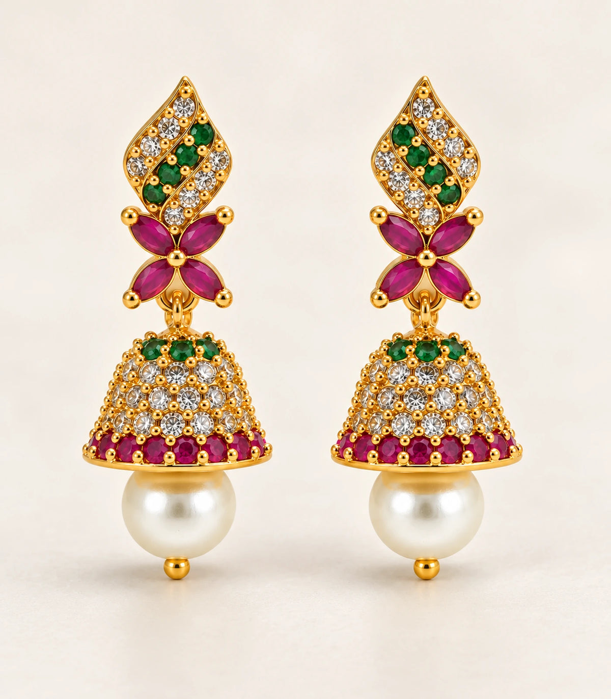 Complete pair of gold-tone green and magenta butterfly pearl-style jhumkas on a warm neutral surface