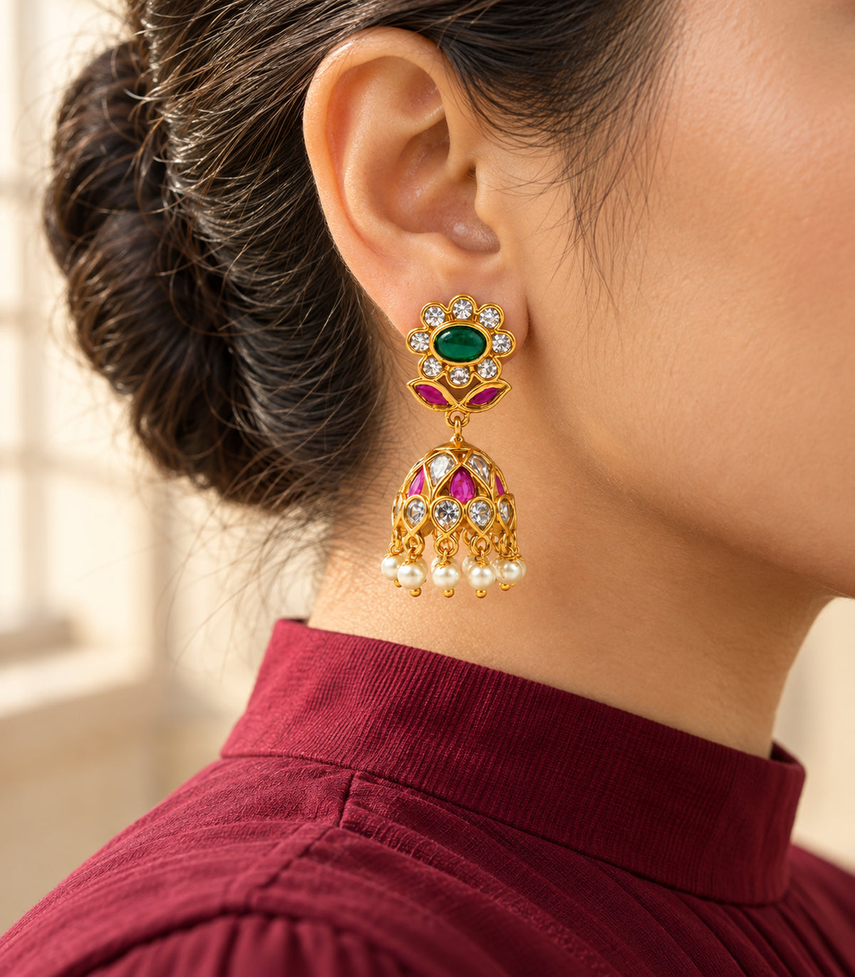 One floral pearl-fringe jhumka worn with a burgundy neckline in warm window light