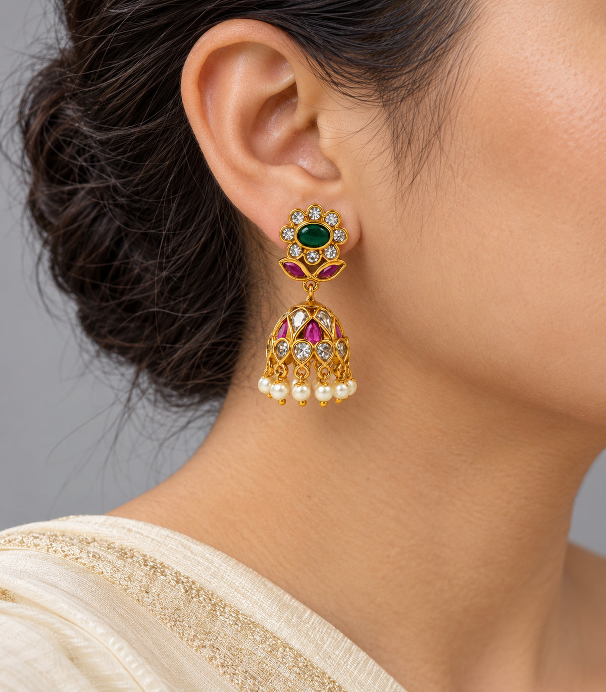Single floral jhumka earring worn with an ivory sari, showing the emerald-green centre, magenta leaves and pearl fringe