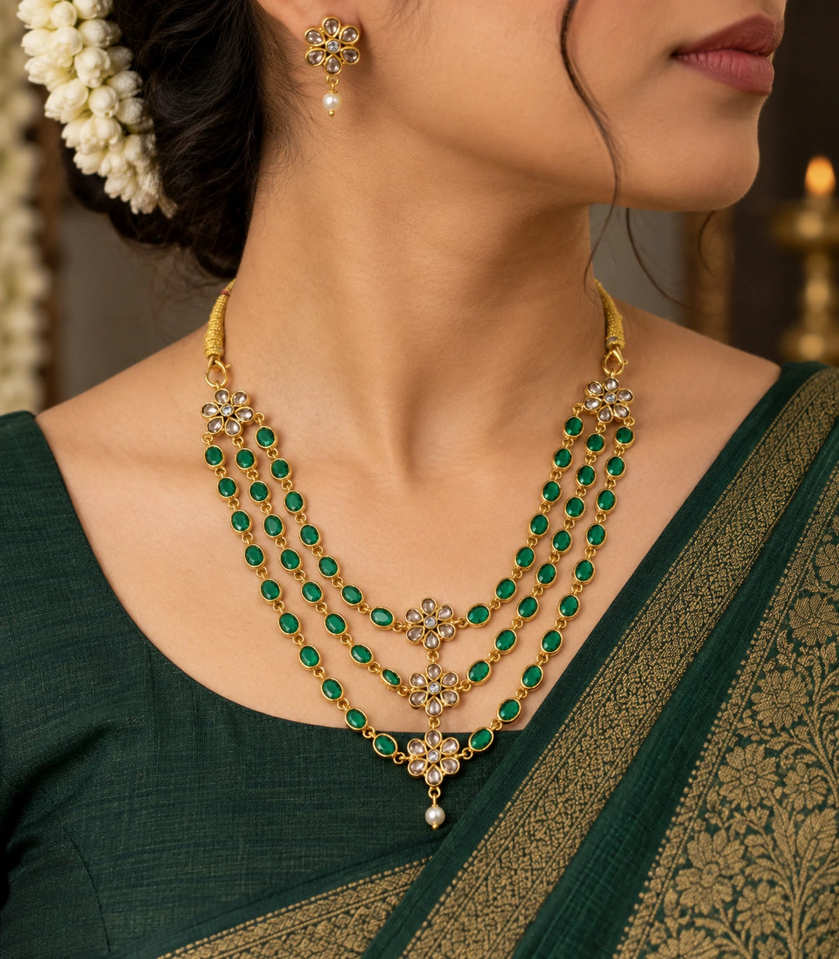 Emerald-green triple-strand floral necklace and one matching white-drop earring worn with a green saree