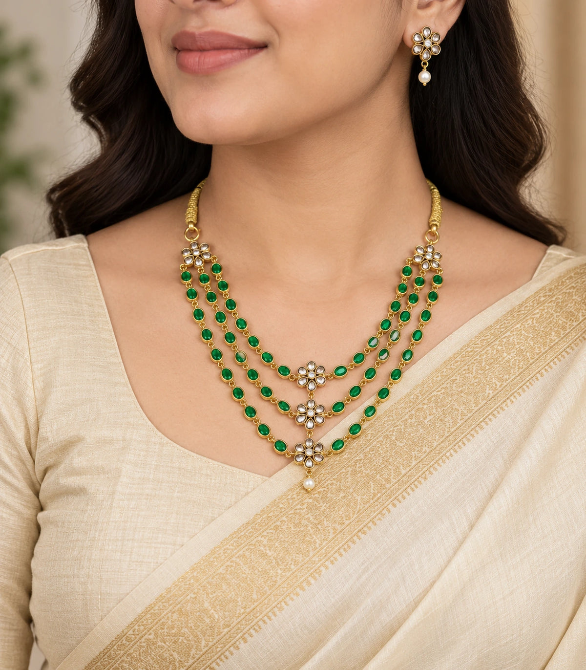 Emerald-green triple-strand floral necklace and one matching white-drop earring worn with an ivory saree