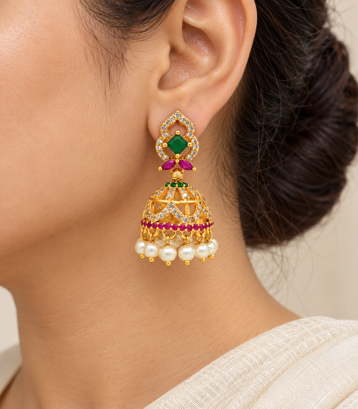 Close view of green diamond-shaped centre, twin magenta leaves and pearl-style fringe on a gold-tone jhumka earring