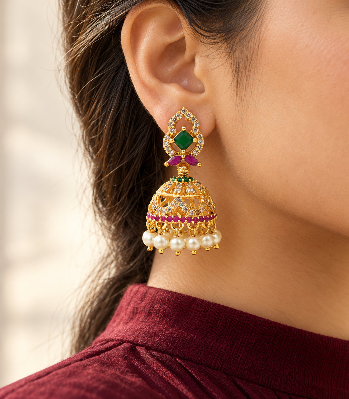 Gold-tone green and magenta jhumka earring worn with a burgundy high-neck outfit