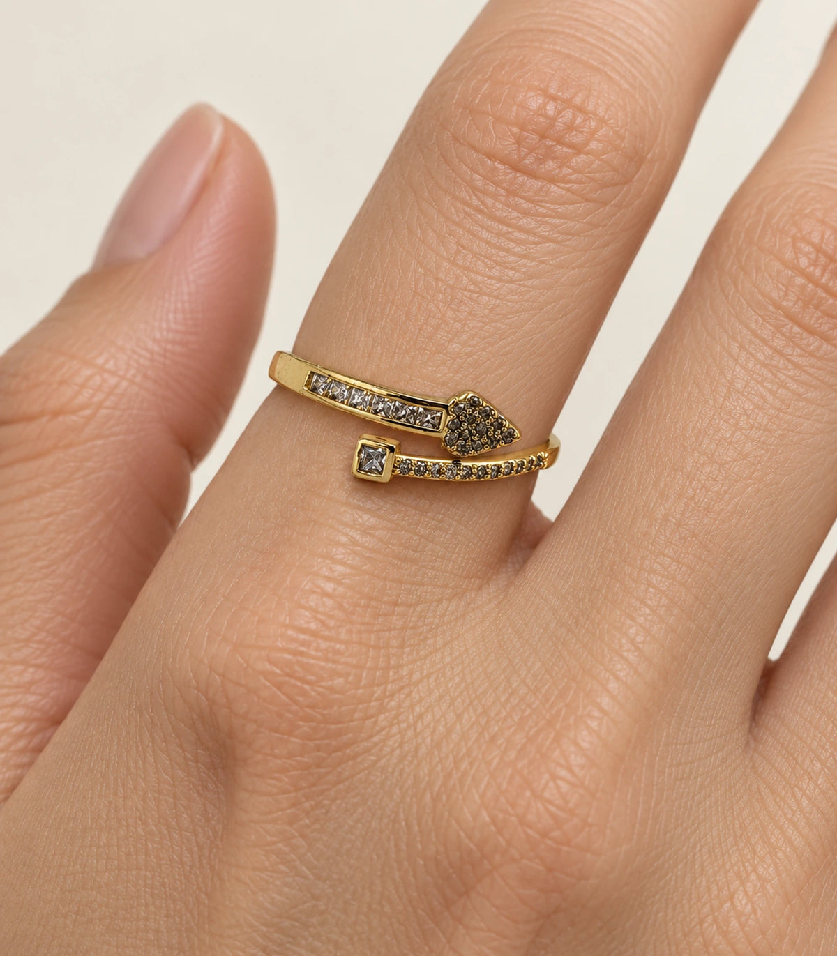 Close-up of gold wrap ring showing heart, square setting and stone rows on a finger