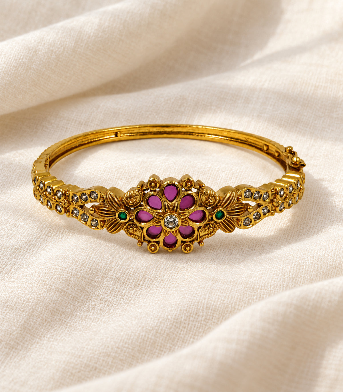 Single gold-tone magenta and green floral bangle in an editorial flatlay