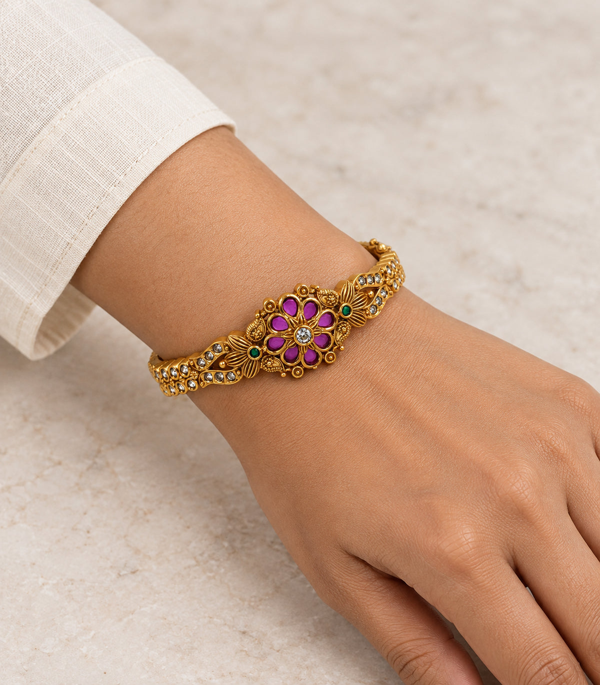 Gold-tone magenta eight-petal and green floral bangle shown on a wrist