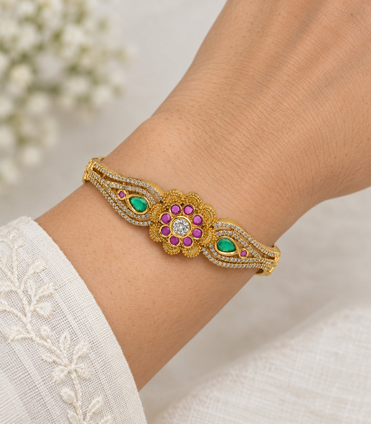 Closeup of the magenta flower and green teardrop details on the gold-tone bangle
