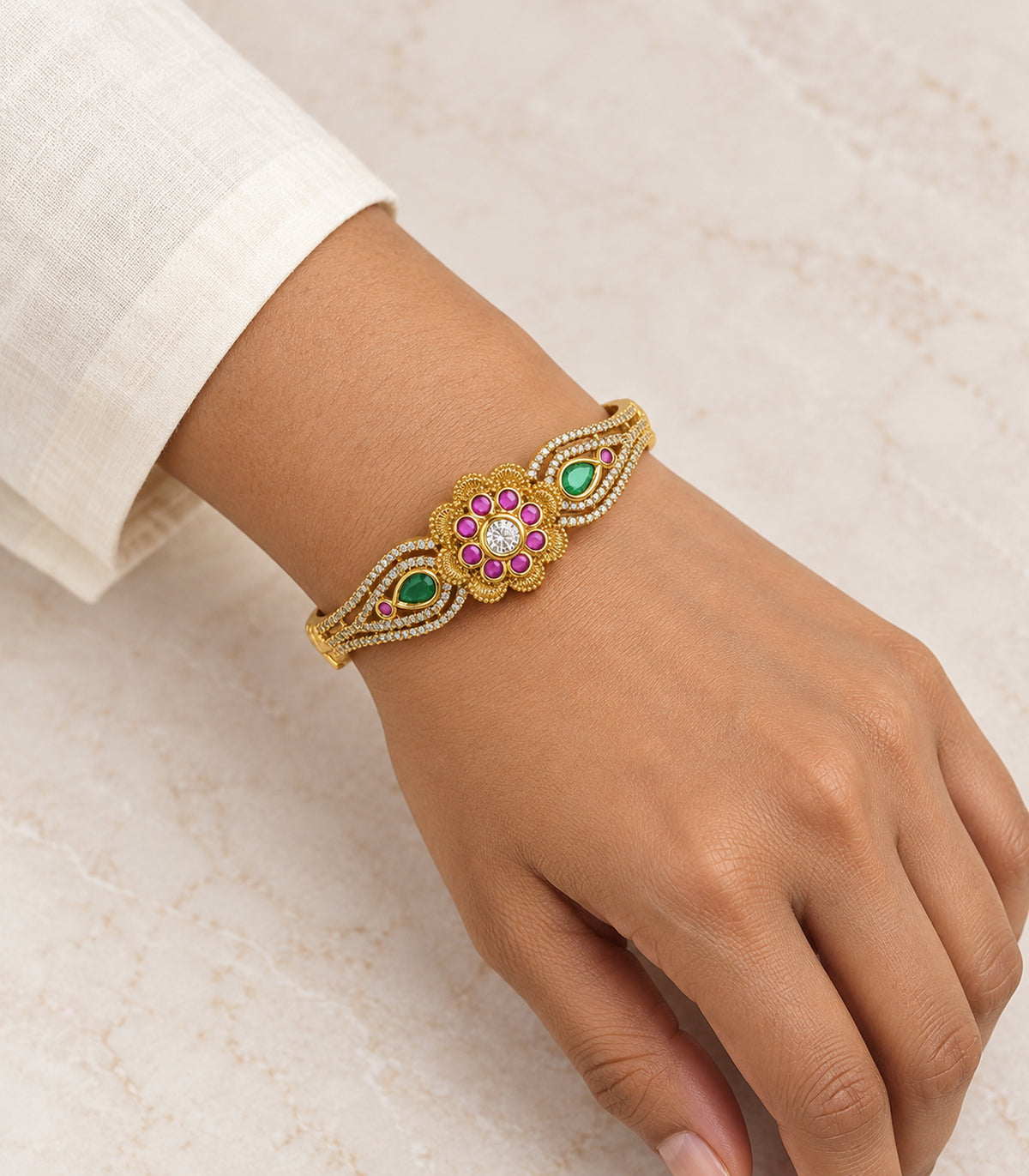 Gold magenta and green teardrop bangle worn on a wrist